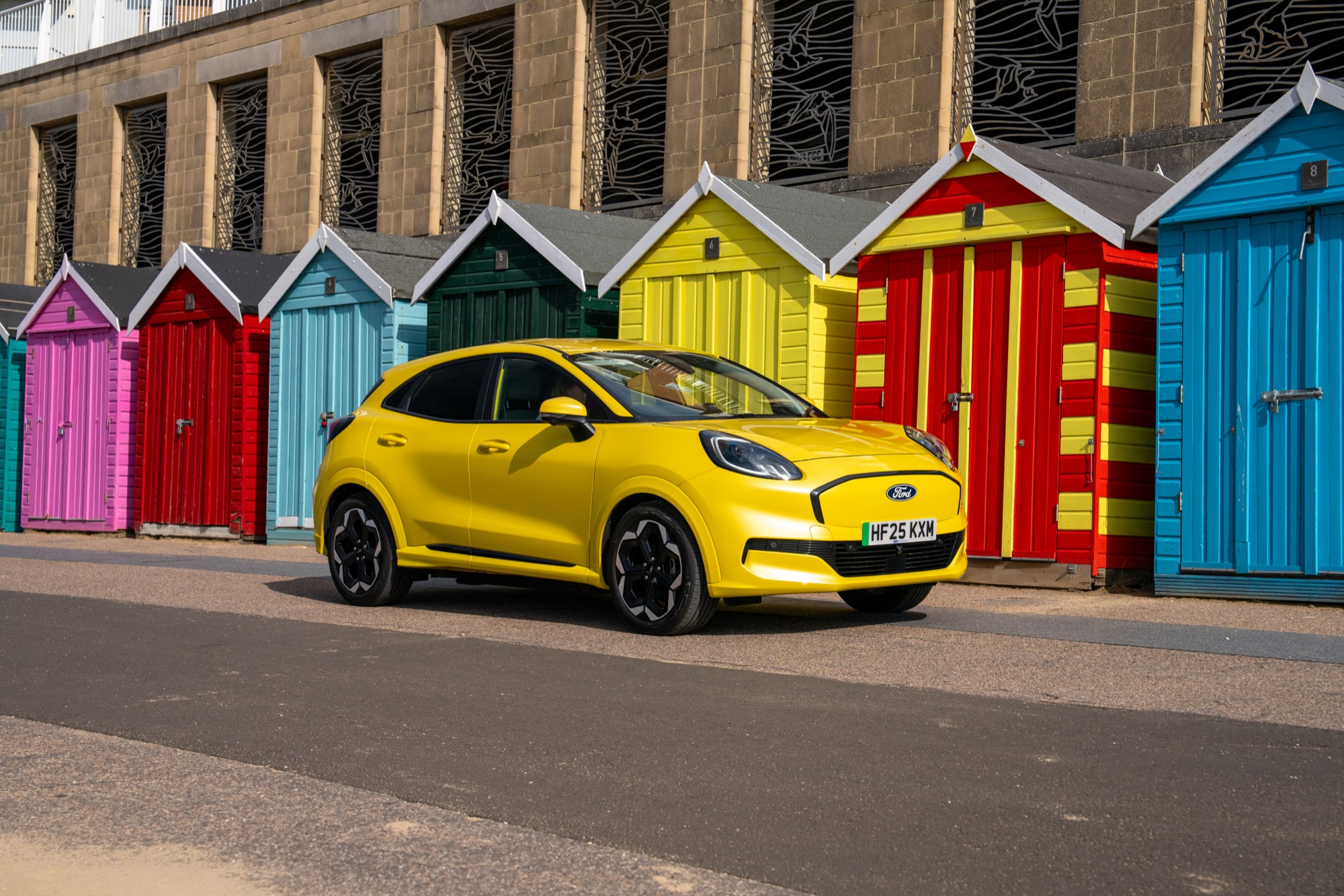 Yellow electric car photographed beside colourful beach architecture